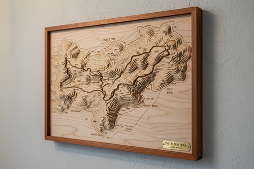 A premium wooden laser-cut cycling route map displayed on a wall, showing a scenic cycling trail with topographic contours and elevation details carved into light birch wood, professional product photography with warm lighting