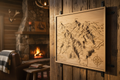 A premium wooden laser-cut hiking trail map displayed in a cozy cabin setting, showing mountain terrain with topographic contour lines carved into natural wood, professional product photography with warm rustic lighting